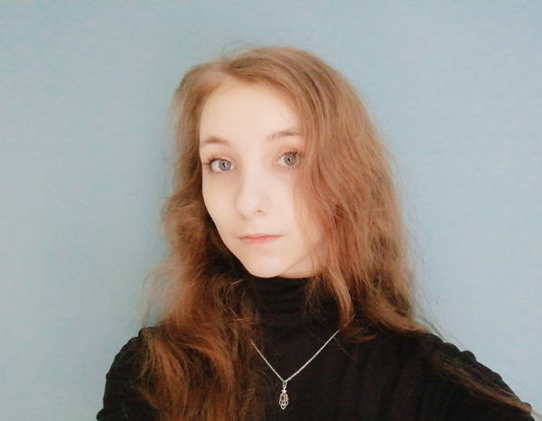 A young white person with long brown hair and blue eyes, wearing a black turtle neck.